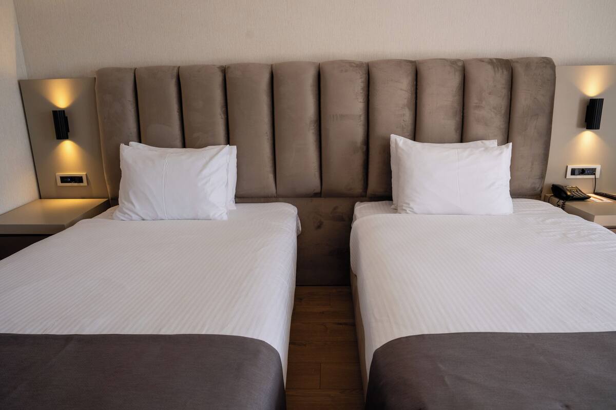 A hotel room with two single beds, a padded headboard, bedside lamps, and a nightstand with a phone.