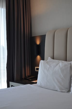 A hotel room with a bed, a nightstand, a lamp, and a view of the city. - Volley Hotel Istanbul (Istanbul)