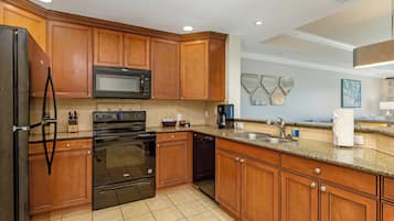 Cocina moderna con gabinetes de madera, refrigerador negro, microondas, horno, lavavajillas y encimera de granito.