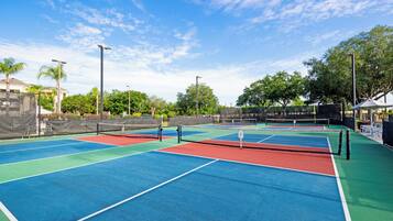 A tennis court with multiple courts, a net, and surrounding fencing.