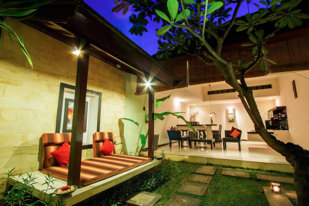 A modern outdoor seating area with a sofa and chairs, a dining table, and a small garden with a tree and plants.