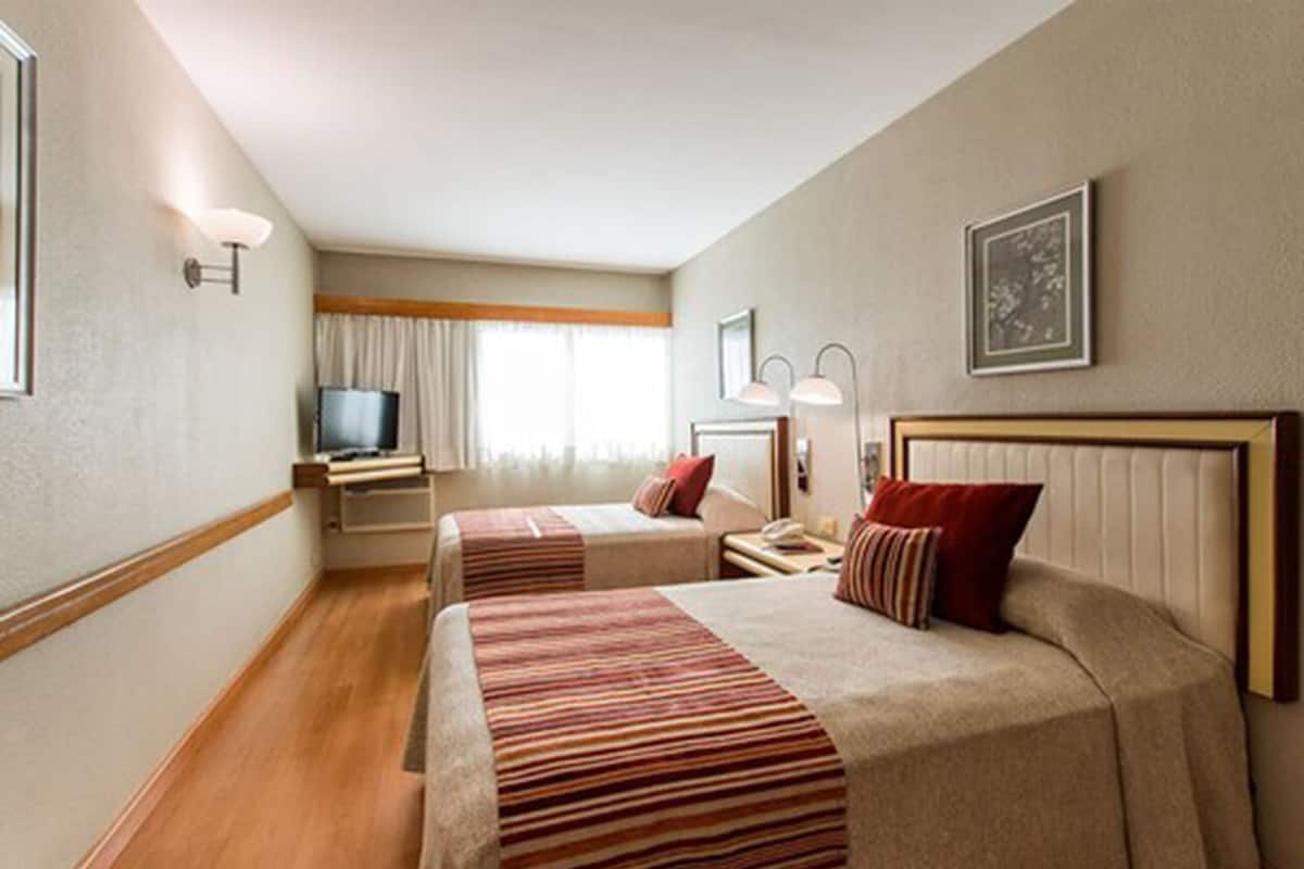 Habitación de hotel con dos camas, televisión, escritorio y ventana con cortinas.