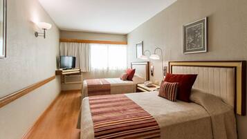 Habitación de hotel con dos camas, televisión, escritorio y ventana con cortinas.