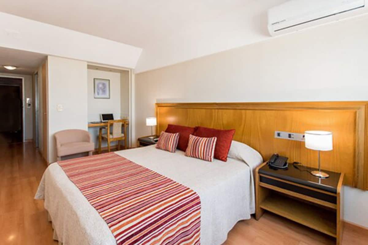 Habitación de hotel con cama, mesita de noche, lámpara y aire acondicionado.