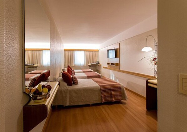 A hotel room with two beds, a television, a bedside table with a lamp, and a fruit bowl. - Hotel Solans Republica (Rosario)