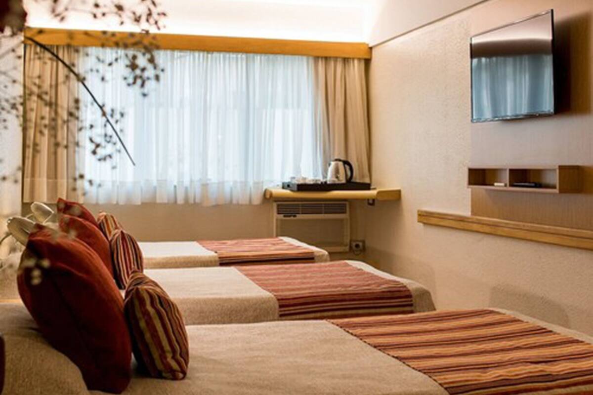 Habitación de hotel con dos camas, televisión, una mesita con hervidor y una ventana con cortinas.