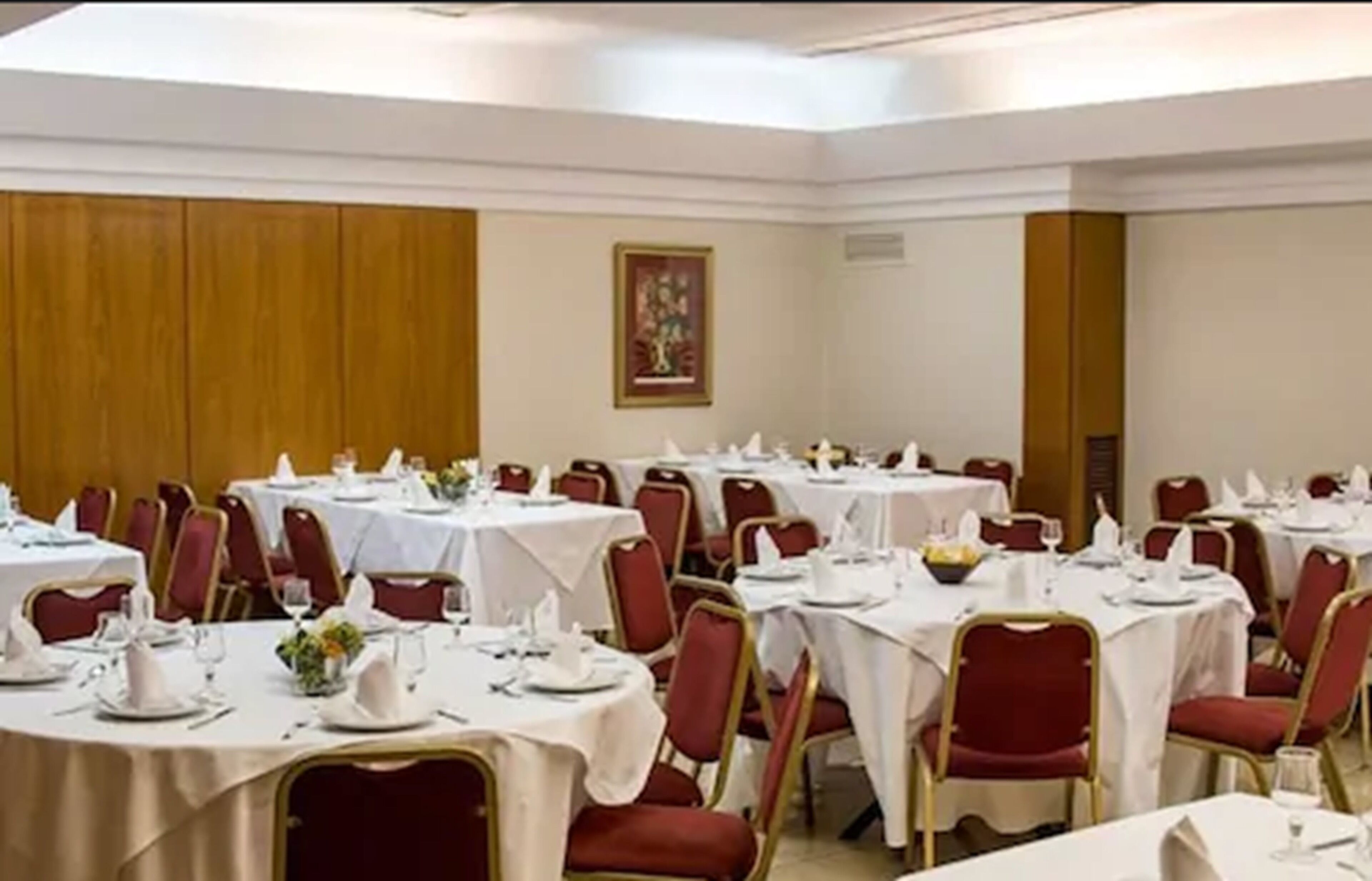 A banquet hall with round tables set for dining, red upholstered chairs, and white tablecloths.