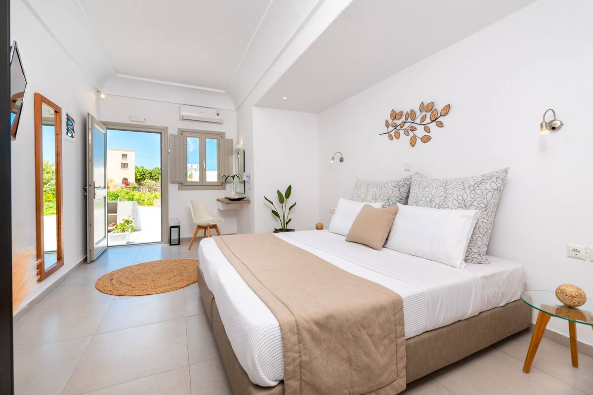 A bedroom with a large bed, a small table, a chair, and a view of the outside.