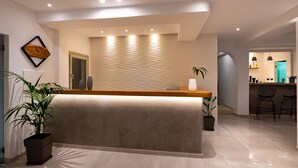 A reception area with a modern design, featuring a reception desk, potted plants, and a wall-mounted light fixture. - Hotel Kalisperis (Santorini)