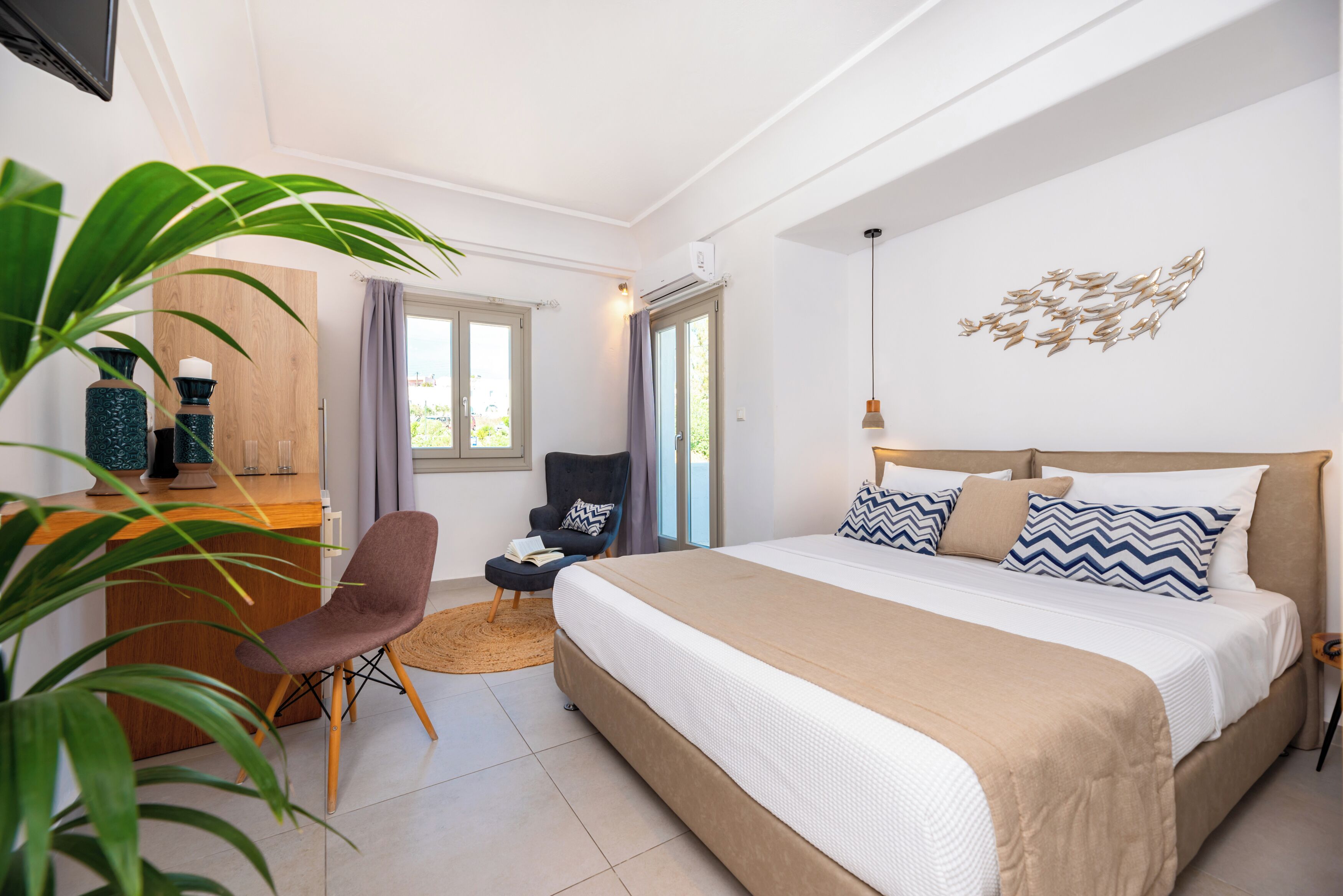 A bedroom with a bed, a desk, a chair, and a large plant.