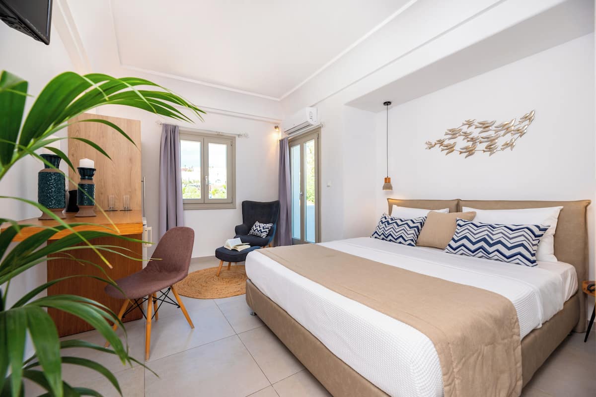 A bedroom with a bed, a desk, a chair, and a large plant.