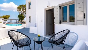 A white building with a pool, two black chairs, and a small table with a vase. - Hotel Kalisperis (Santorini)