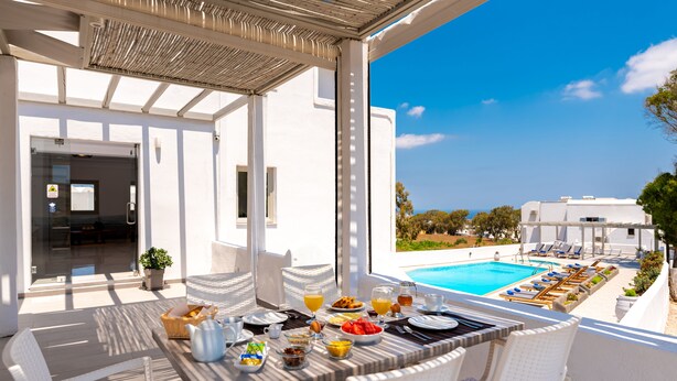 A breakfast table with breakfast items, a pool, and lounge chairs in the background. - Hotel Kalisperis (Santorini)