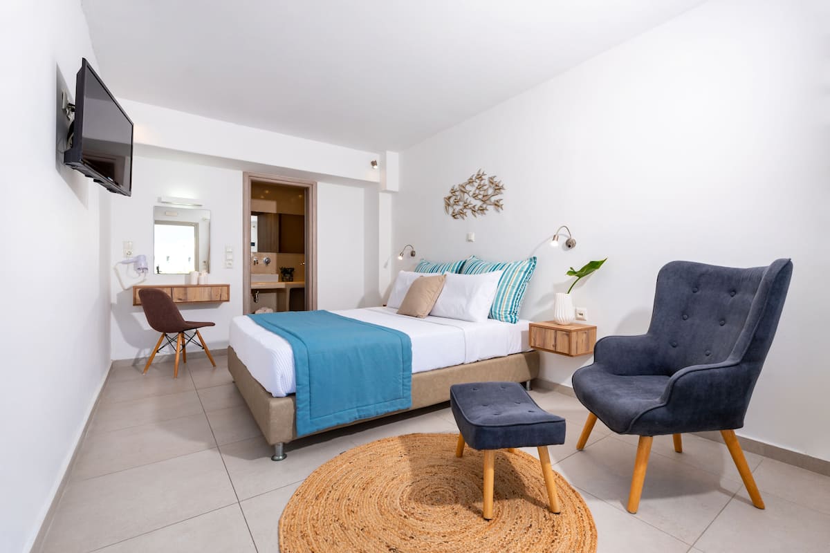 A modern bedroom with a bed, a desk, a chair, and a TV.