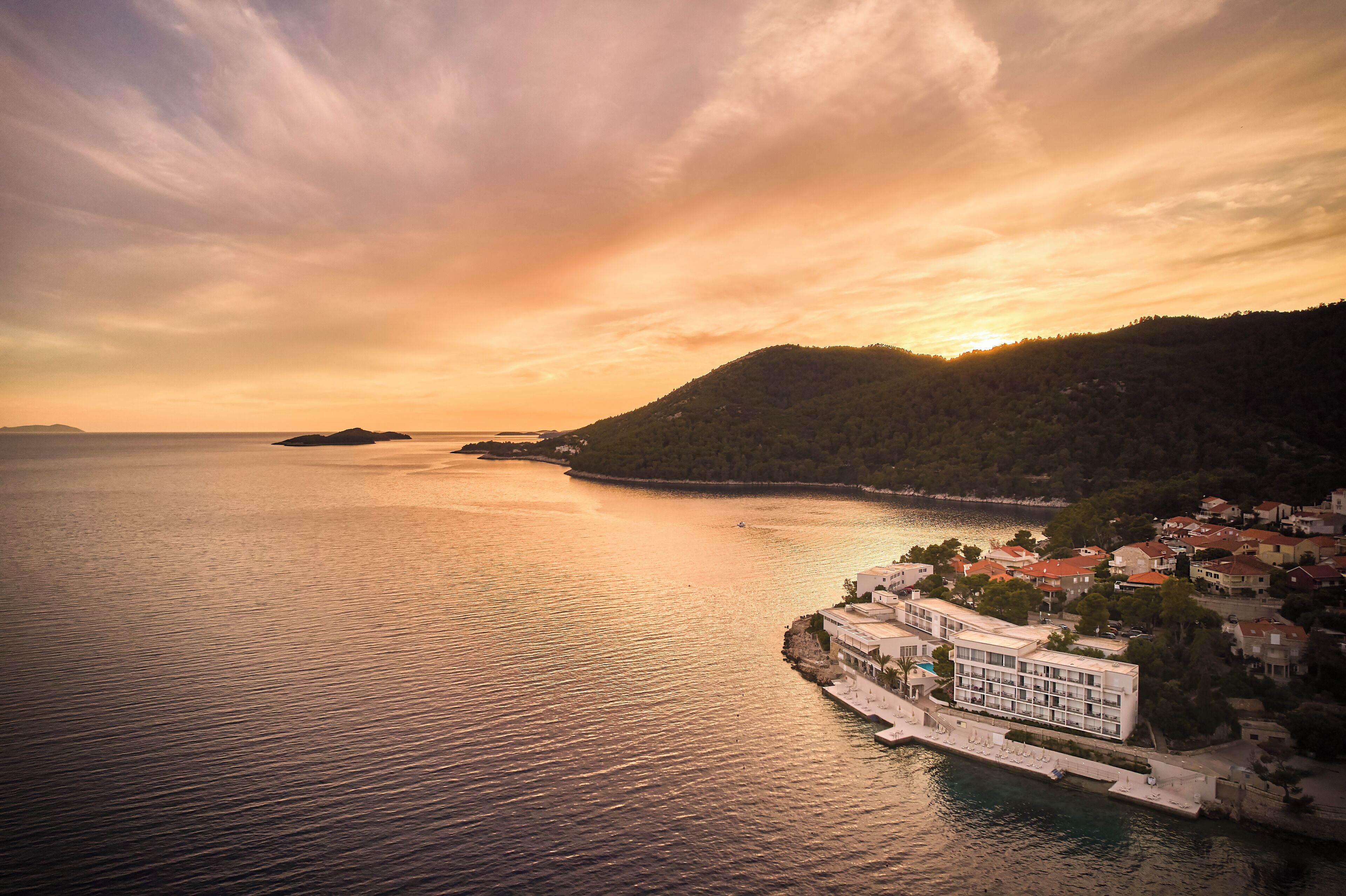 A coastal hotel with a waterfront view, featuring a large building with multiple floors and a long pier extending into the sea.
