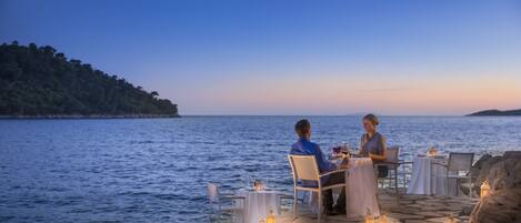 A couple dining at a table by the sea with a view of the water and a distant island.