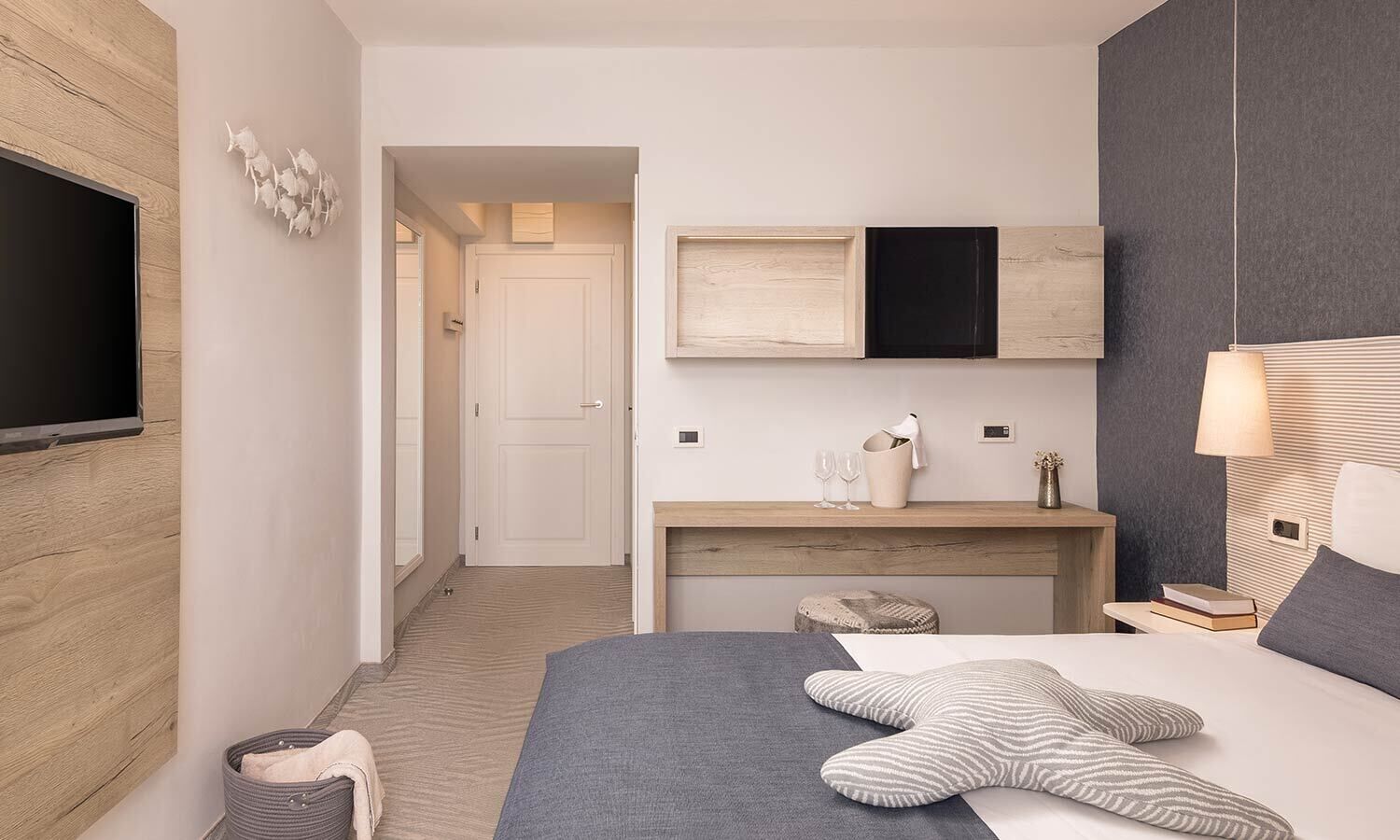 Una camera d'albergo moderna con un letto grande, una televisione a schermo piatto montata a parete, una toeletta in legno e un comodino con una lampada.
