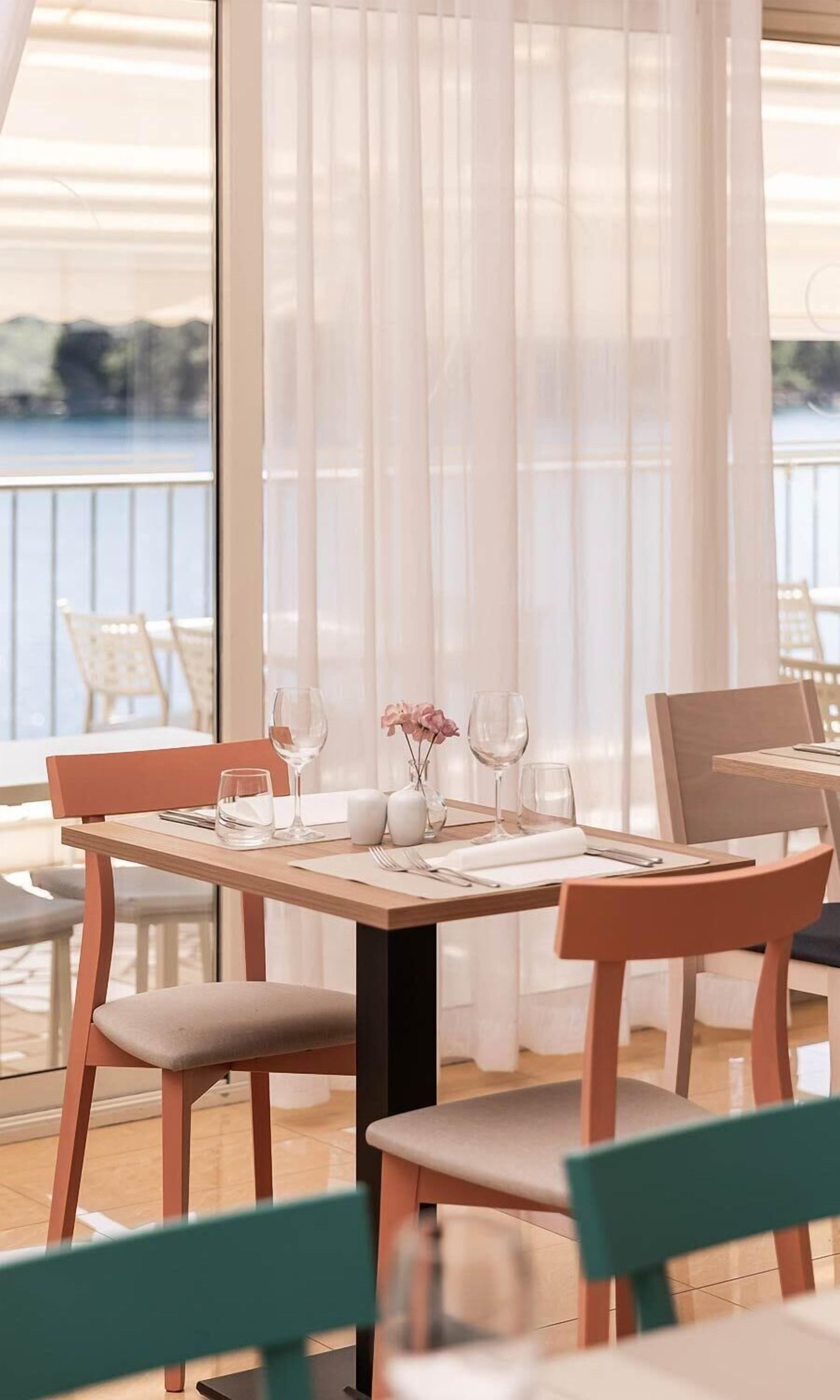 Zona de dinar amb taula per a quatre, cadires i vista al mar a través de cortines transparents.