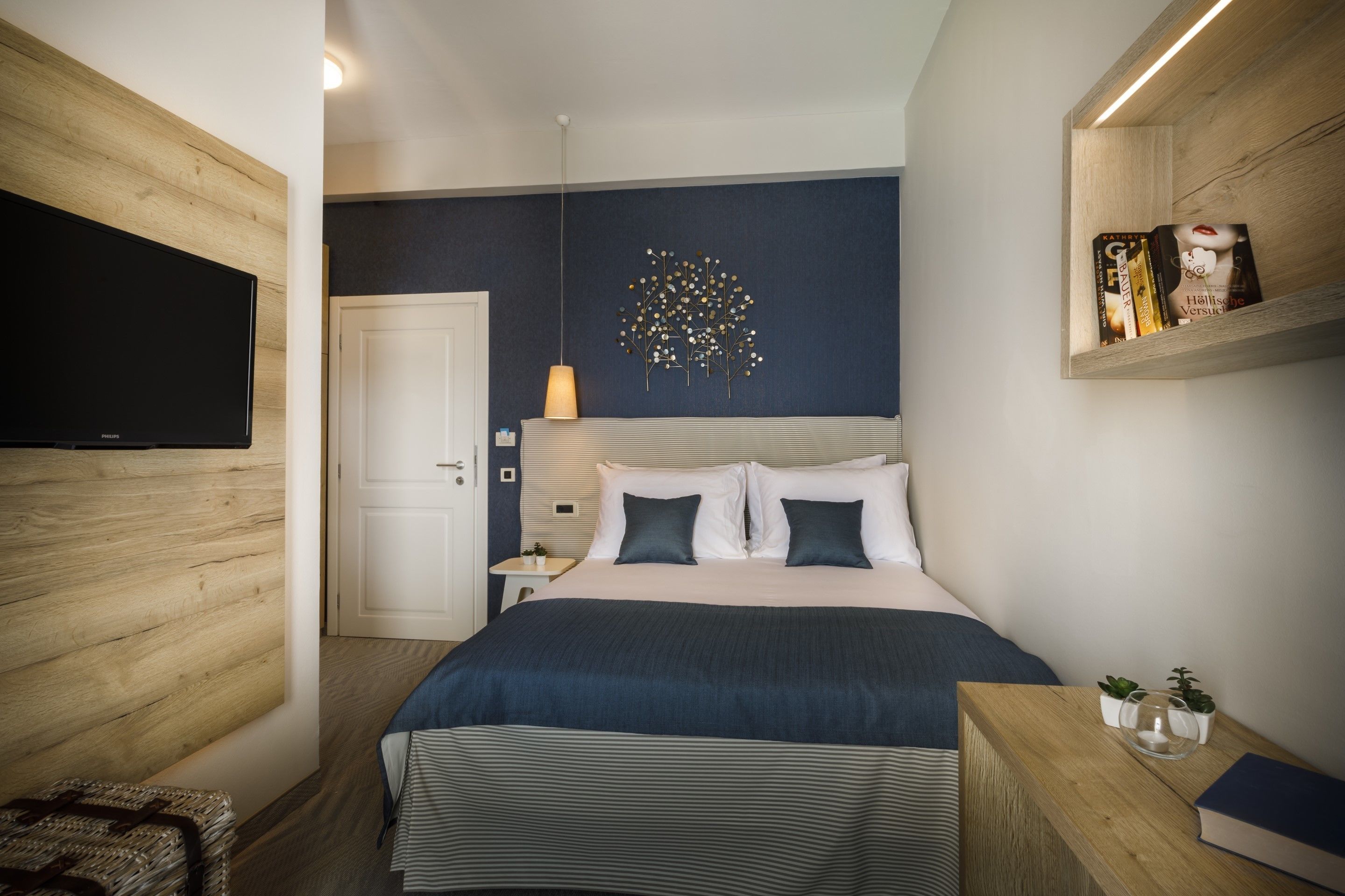 A modern bedroom with a bed, bedside tables, a TV, and a wall-mounted shelf with books.