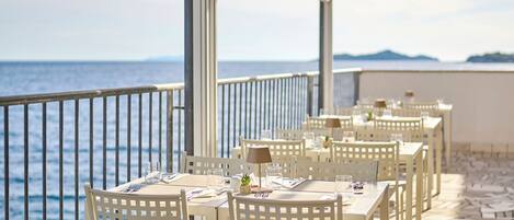 Una terraza con mesas y sillas blancas, con vista al mar.