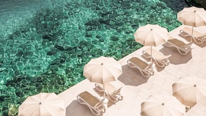 A poolside area with clear water, lounge chairs, and umbrellas. - Aminess Lume Hotel (Smokvica)