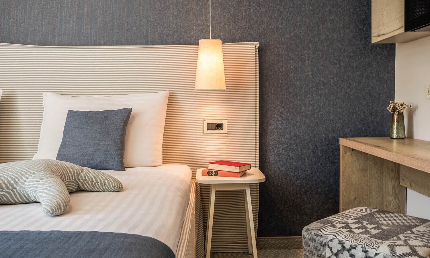 A neatly arranged hotel room with a bed, bedside table, and a small stool.
