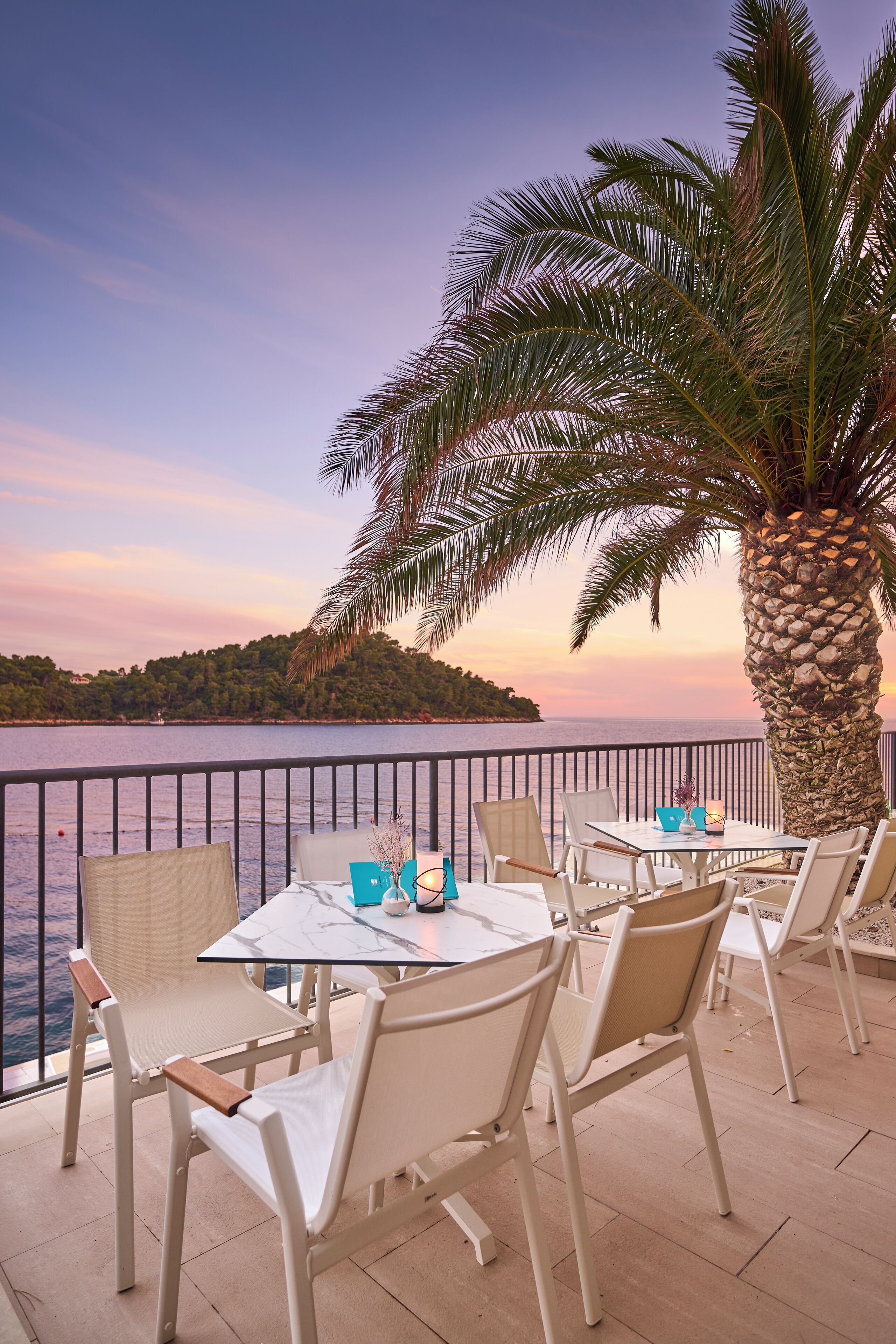 Eine Terrasse mit Tisch und Stühlen, mit Blick auf ein Gewässer und ein entferntes Land.