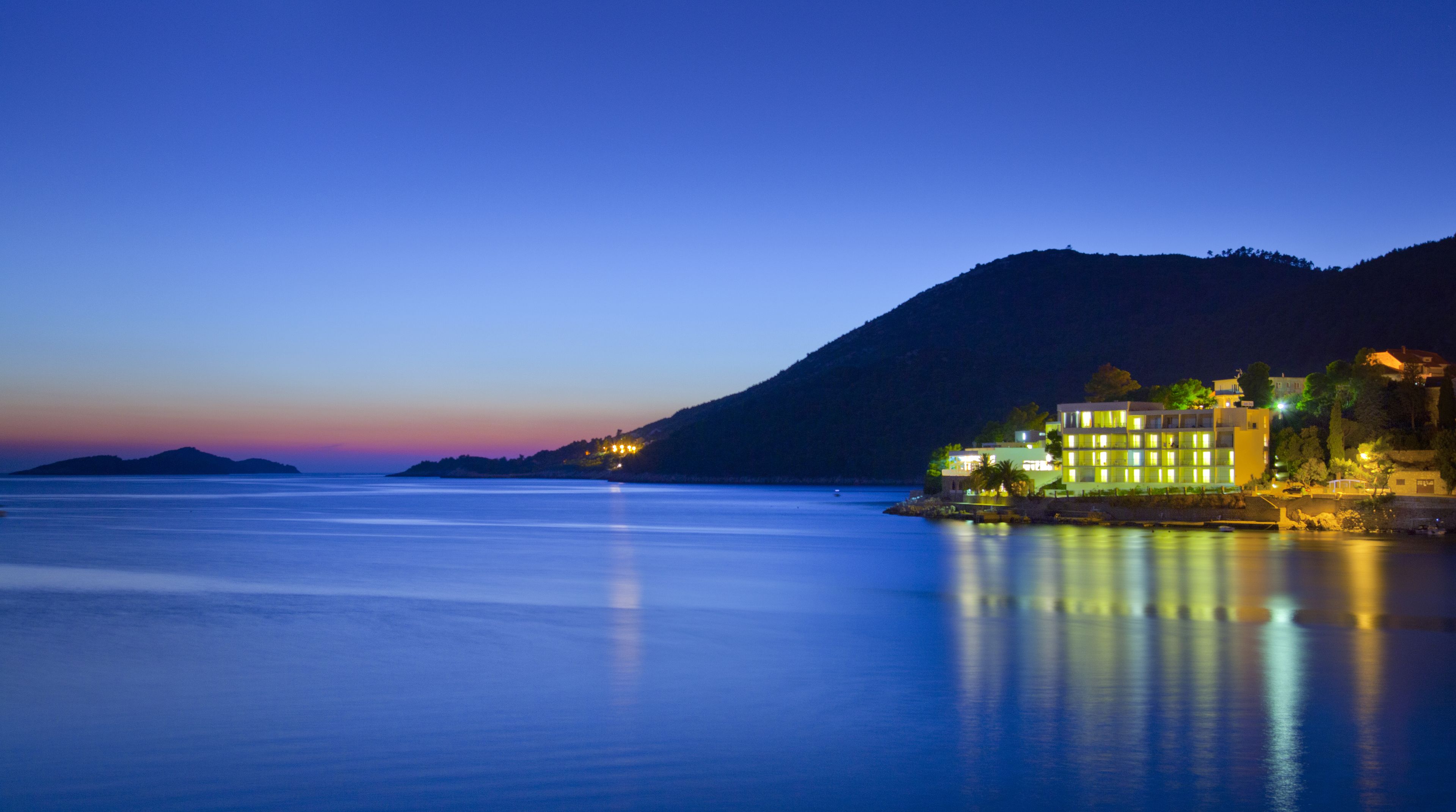 A coastal hotel with multiple buildings, a calm sea, and a mountain in the background.