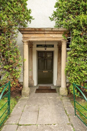 Stately entrance with a classical design, featuring a dark green door and stone pathway.