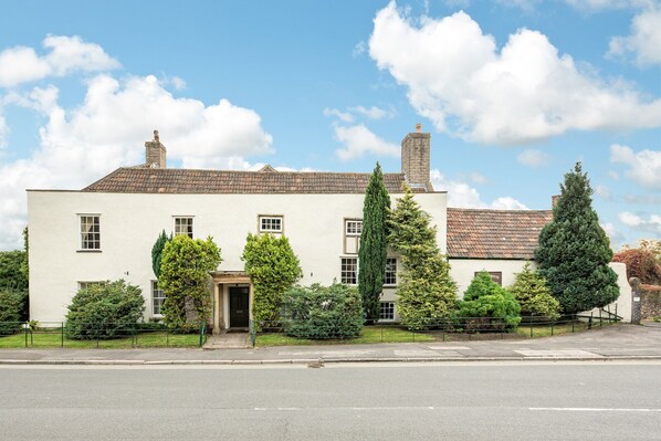 Stately building with a central entrance, flanked by windows, set amidst a well-manicured lawn and mature trees.