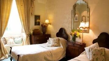Une chambre avec deux lits, un miroir, une commode et une fenêtre avec des rideaux.