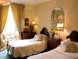 A room with two beds, a mirror, a dresser, and a window with curtains.
