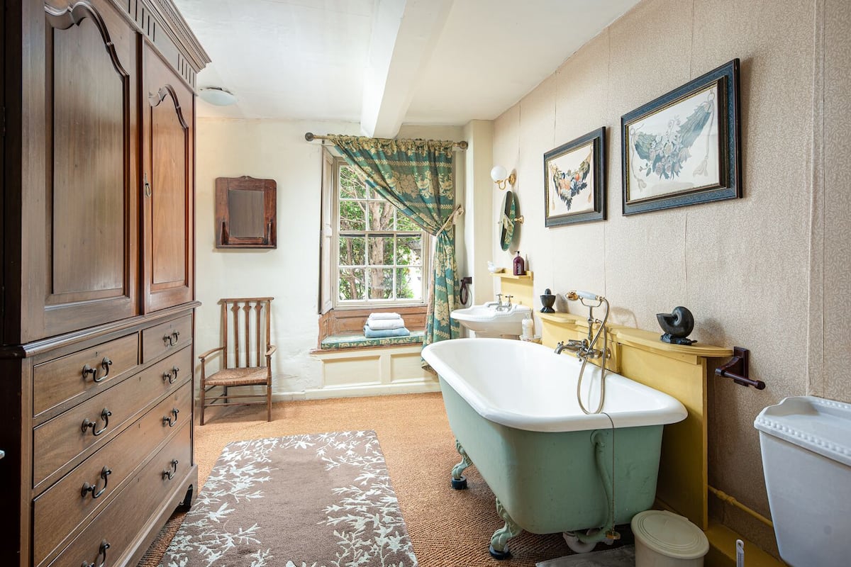 A vintage bathroom with a clawfoot bathtub, wooden cabinetry, and a window with floral curtains.