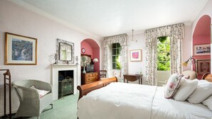A bedroom with a bed, a chair, a dresser, a mirror, and a fireplace. - Compton House (Axbridge)
