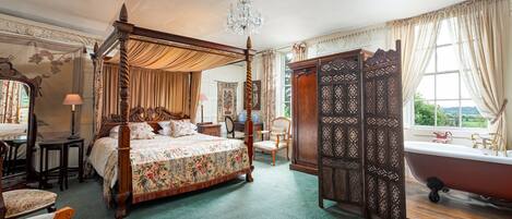 A spacious bedroom with a four-poster bed, a clawfoot bathtub, and a large window with curtains.