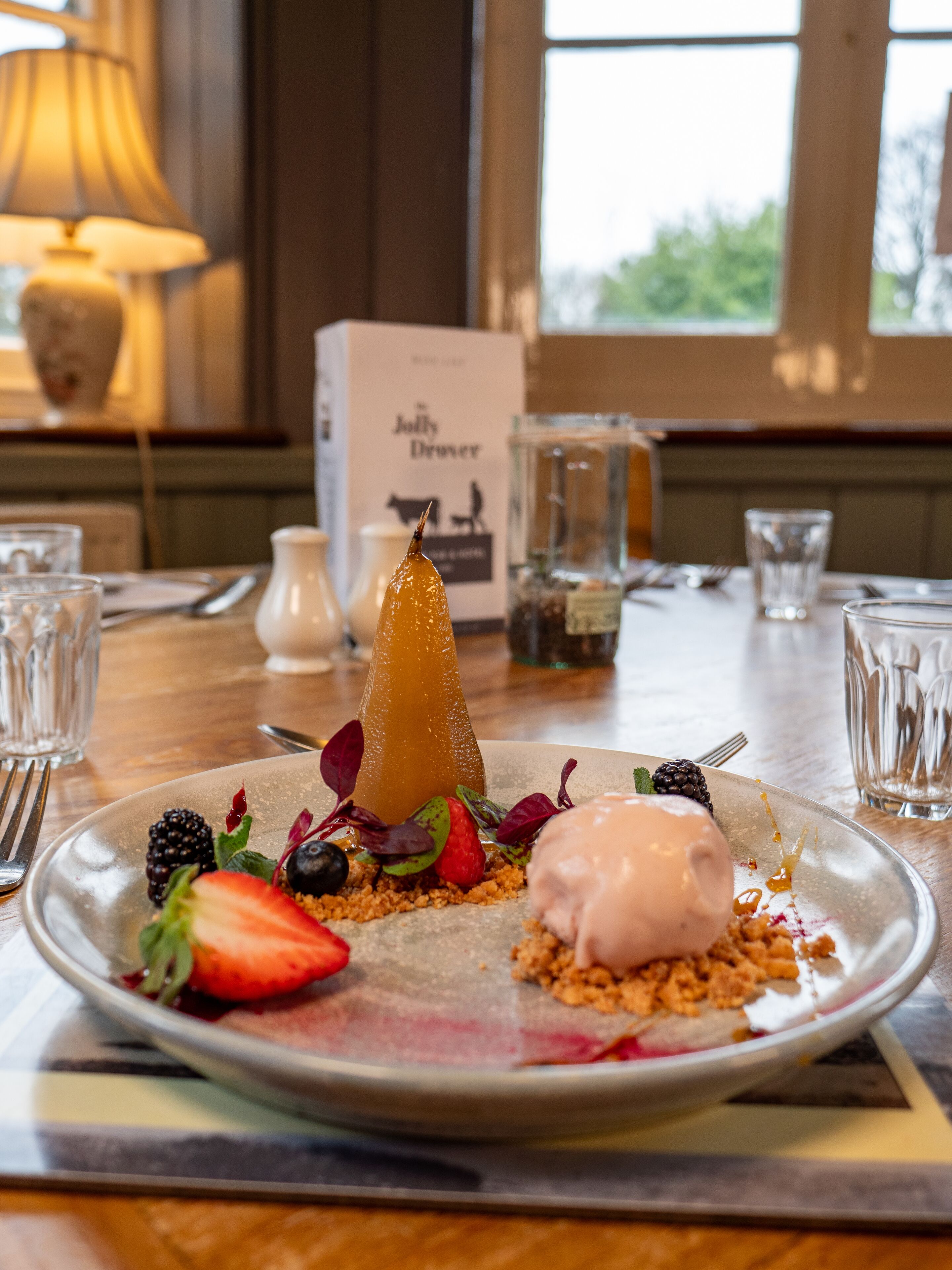 A dessert plate with a pear, berries, and a scoop of ice cream on a table in a restaurant.