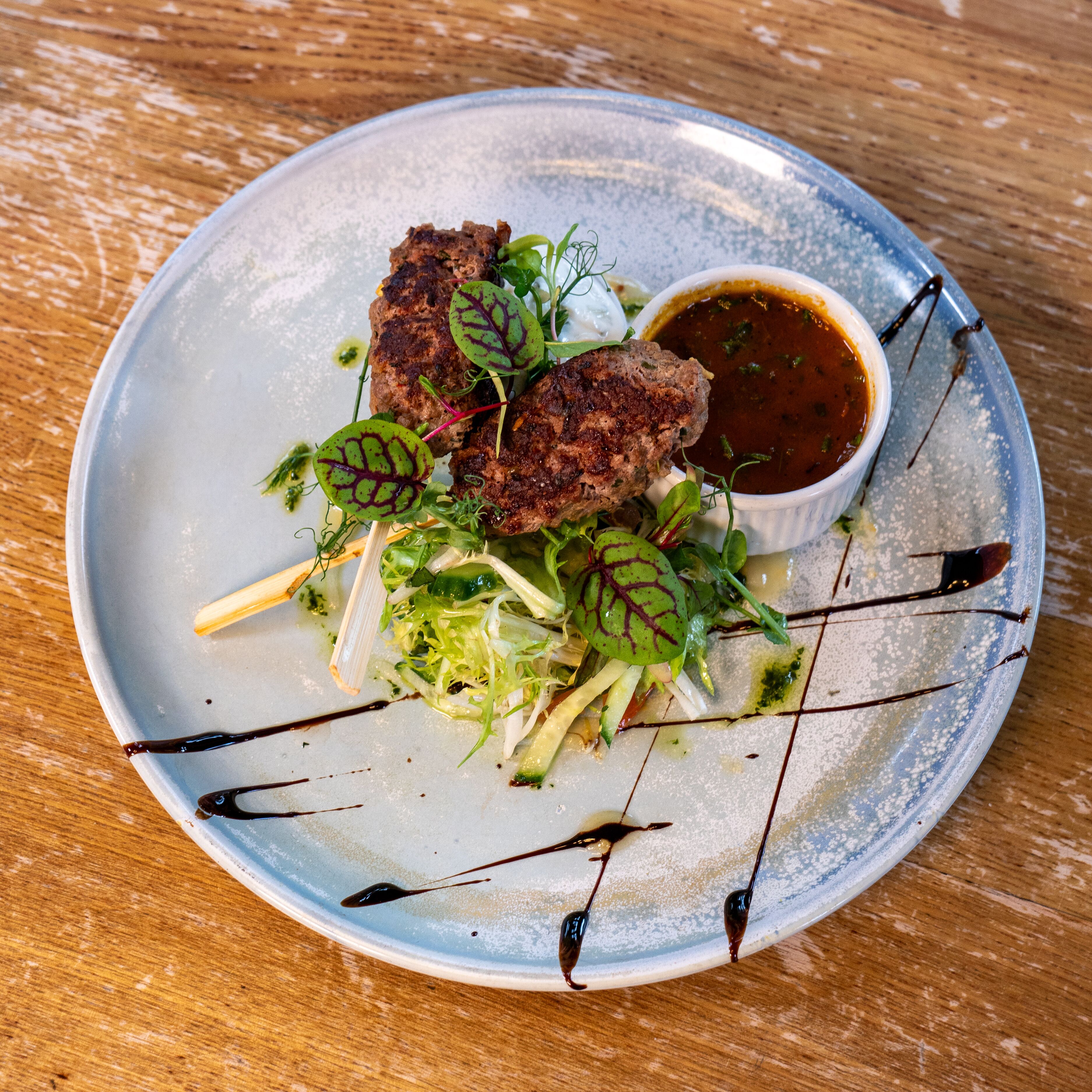 A plate with food, including meat patties and greens, on a wooden table.