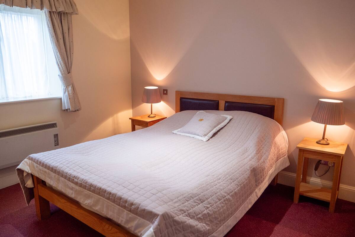 A neatly made bed with a white duvet, two bedside lamps, and a window with curtains.