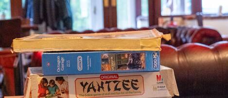 A stack of board games on a wooden table in a room with a high ceiling and arched windows.