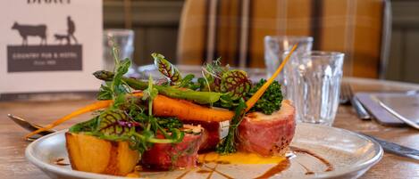 A plate of food with vegetables and meat, a glass of water, and a menu on the table.