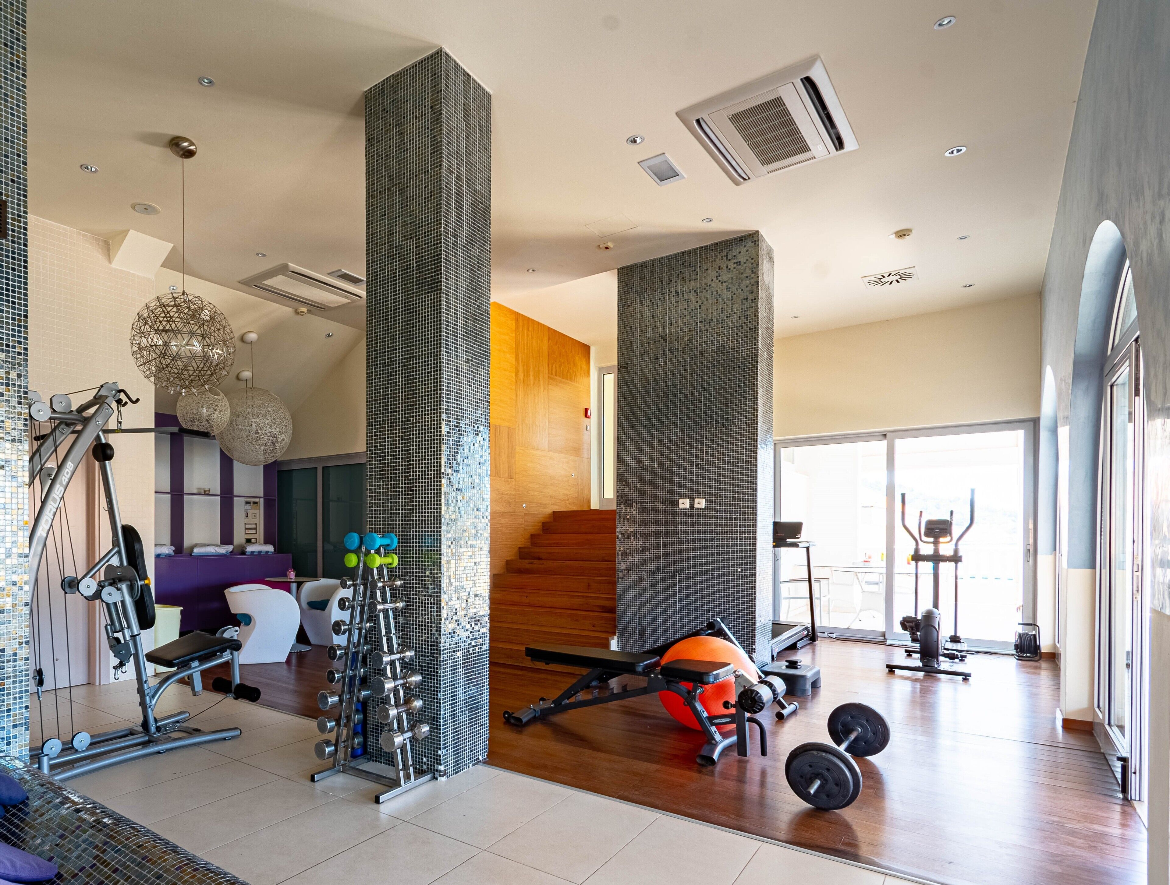 A modern gym with exercise equipment, a staircase, and large windows.