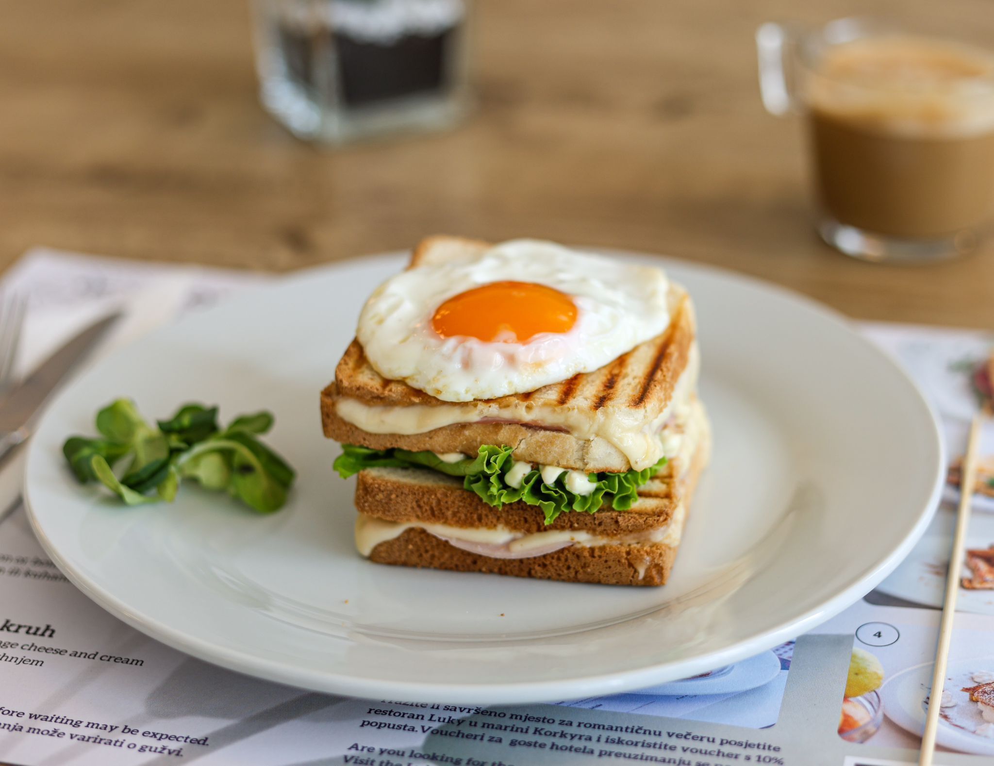 Un sandwich avec un œuf au plat, servi sur une assiette blanche, accompagné d’une tasse de café et d’un menu.