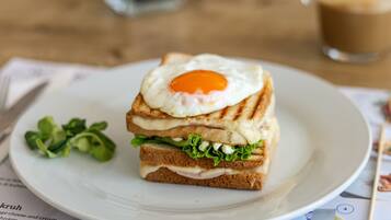 Un sandwich avec un œuf au plat, servi sur une assiette blanche, accompagné d’une tasse de café et d’un menu.