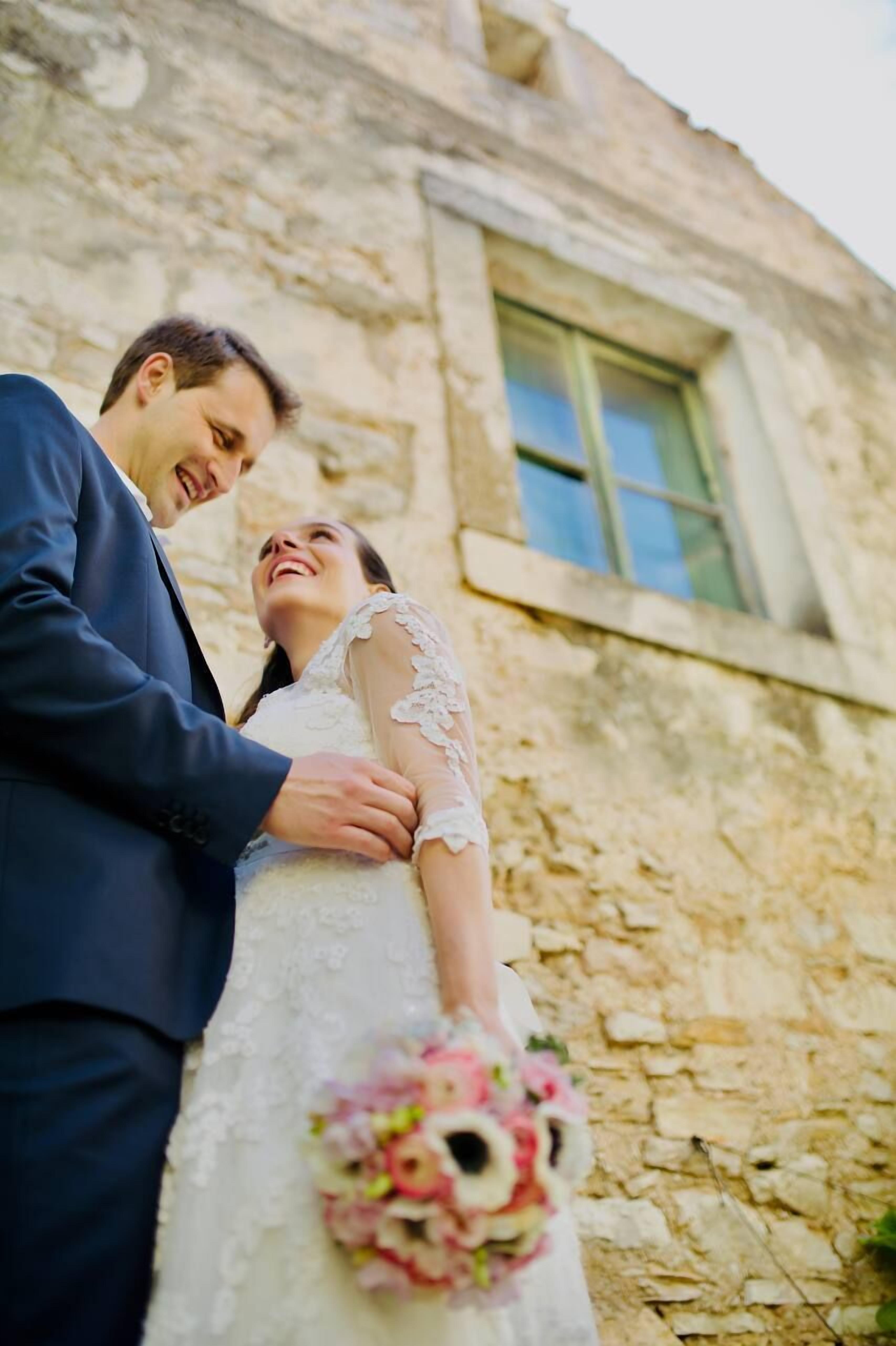 A couple embracing in front of a stone building with a window.