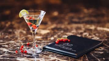 A martini glass with a lime wedge and red berries on a marble surface, next to a black notebook.