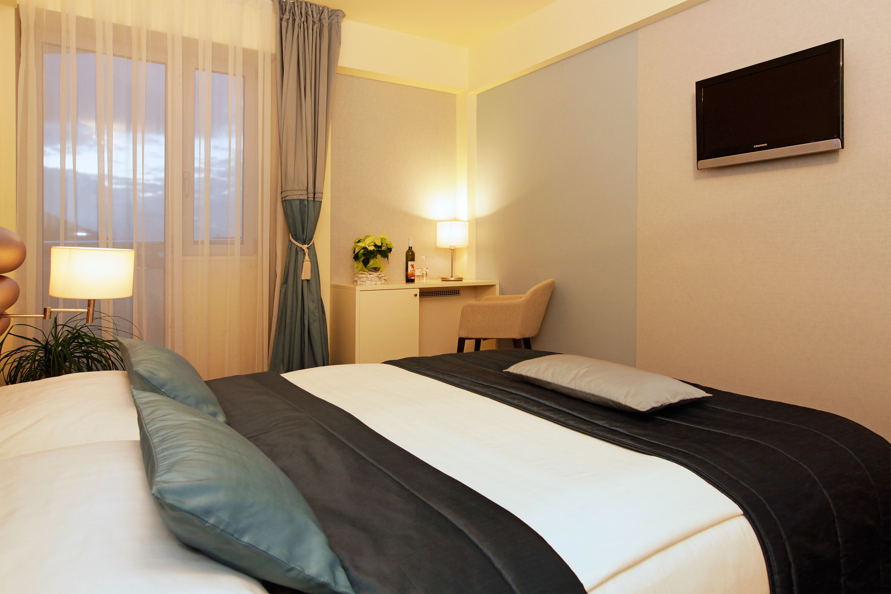 A hotel room with a bed, a desk, a chair, a TV, and a lamp.