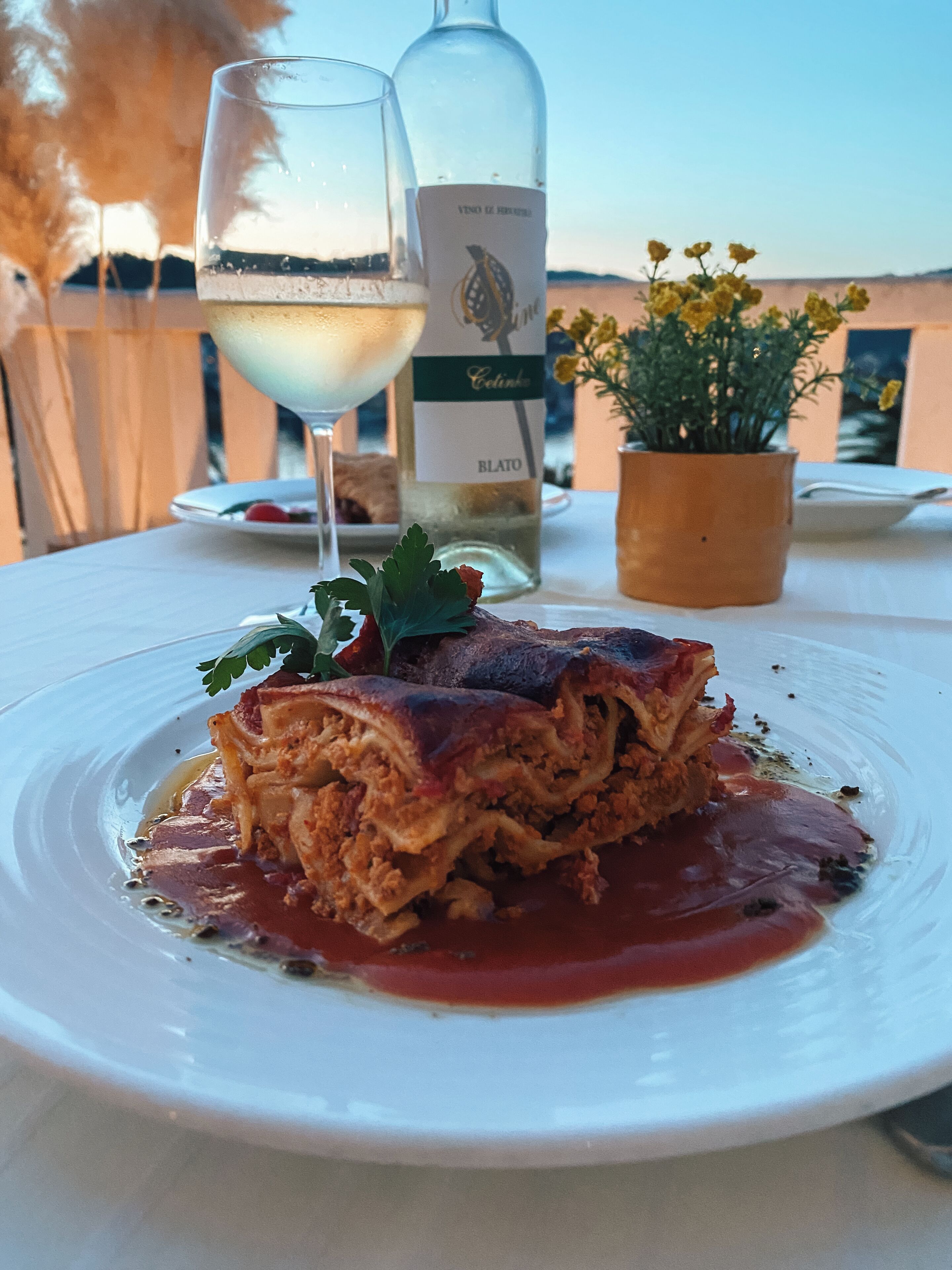 Ein Teller mit Essen, eine Weinflasche und ein Glas Weißwein auf einem Tisch im Freien.