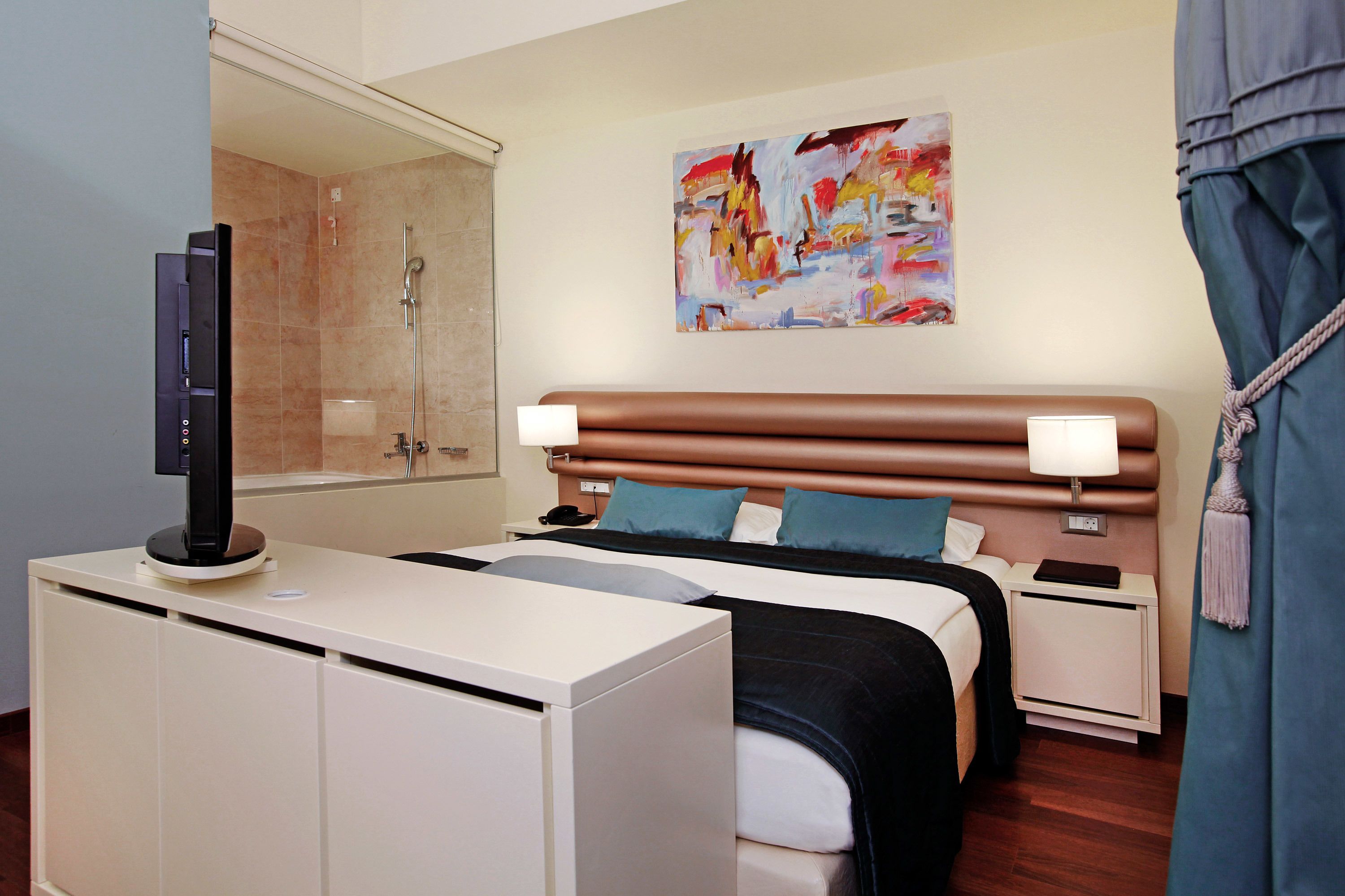 Ein Hotelzimmer mit Bett, Nachttischen, Fernseher, Dusche und einem Bild an der Wand.