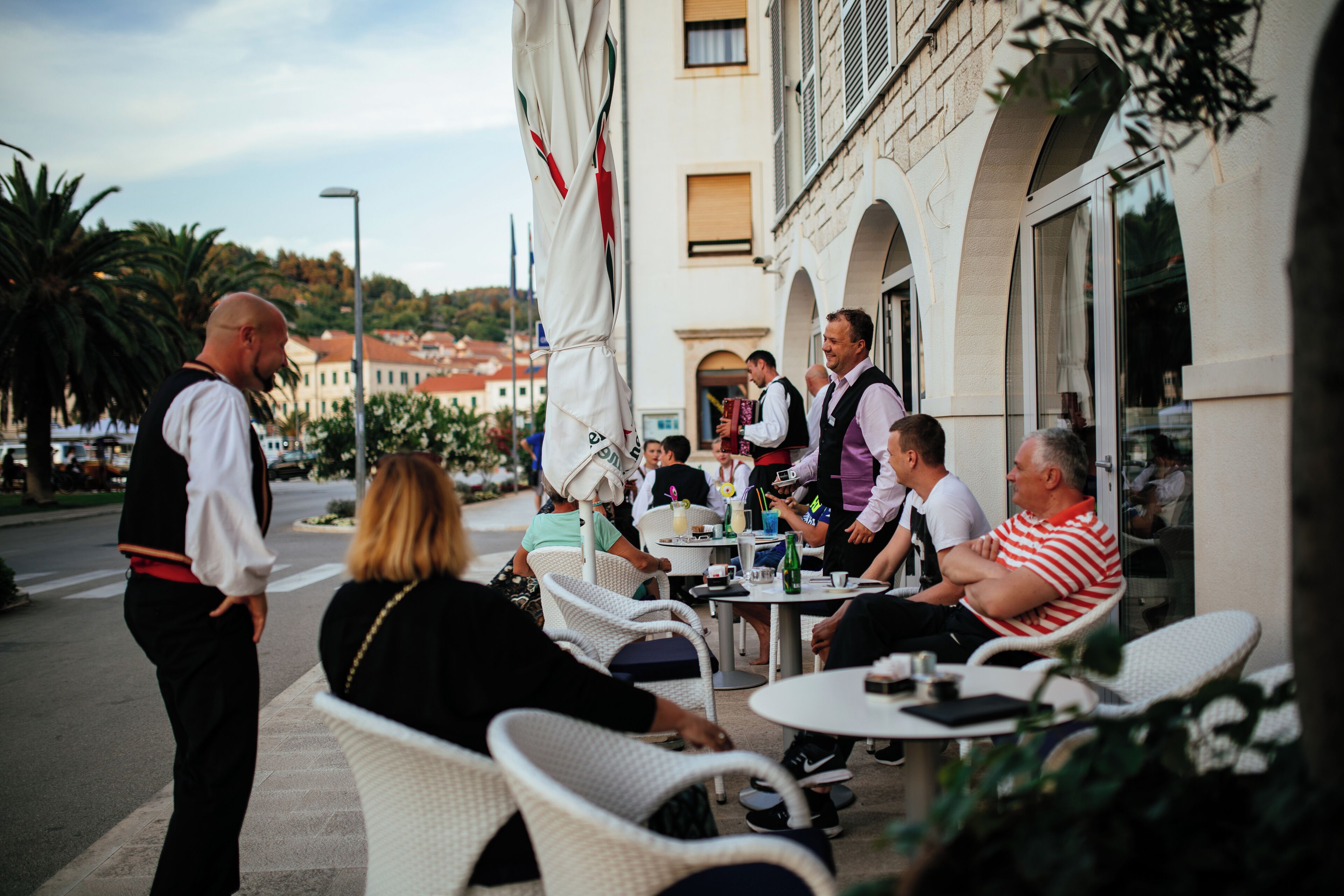 A group of people seated at outdoor tables with white wicker chairs, engaged in conversation.