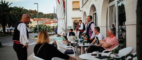 A group of people seated at outdoor tables with white wicker chairs, engaged in conversation.